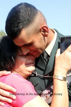 a man and woman hugging each other while holding a cell phone up to their face