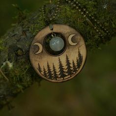 a necklace with an image of the moon and trees on it hanging from a tree branch