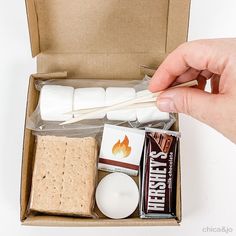 someone is holding marshmallows and sticks in a box with other food items