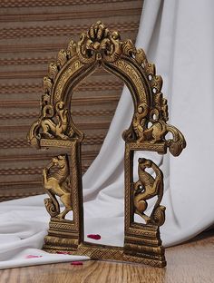 an ornately decorated gold arch stands on a wooden floor next to a white curtain