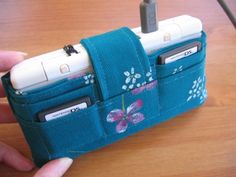 a hand holding a cell phone holder made out of blue fabric with flowers and butterflies on it