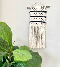 a white wall hanging with black and white crochet on it next to a potted plant