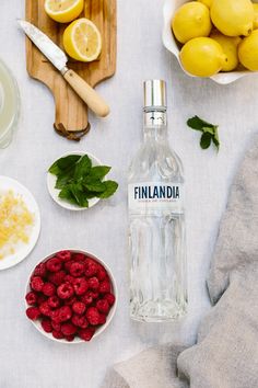 a table topped with bowls of raspberries and lemons next to a bottle of finlandna