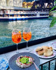 two plates with food and drinks sitting on a table next to the water