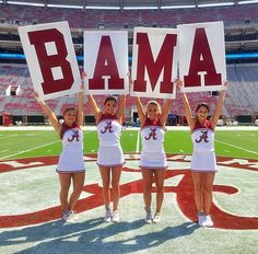 three cheerleaders holding up signs in front of an empty stadium