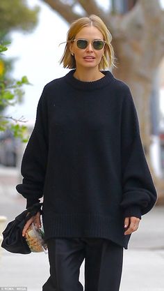 a woman in black sweater and pants walking down the street