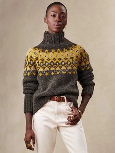 a woman standing in front of a white wall wearing a sweater and pants with yellow flowers on it