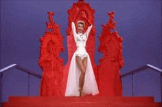 a woman in a white dress standing on top of a red stage with her arms up