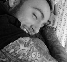 a man with tattoos on his arms and chest laying down next to a wall, looking at the camera