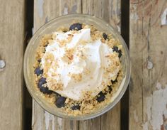 a dessert in a glass bowl on top of a wooden table with white frosting and blueberries