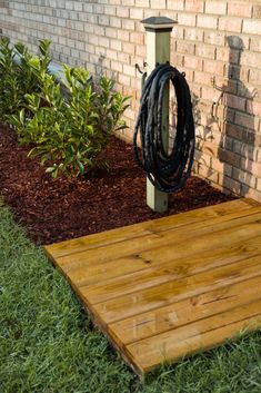 a wooden platform with a black rope on it in front of a brick wall and green grass