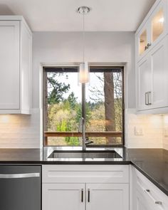 a kitchen with white cabinets and black counter tops next to a large window that looks out onto the woods