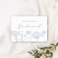 the bridesmaid card is laying on top of a blanket with flowers and greenery