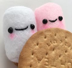 two marshmallows and a cookie on a white surface with black eyes, one is pink and the other is white