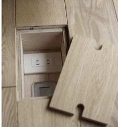 an open wooden box on the floor with some electrical plugs in it