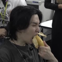 a man with black hair eating a banana in an office setting while another person looks on