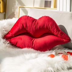 a red pillow sitting on top of a white fur covered bed next to a window