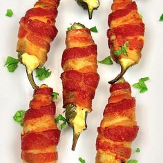 bacon wrapped jalapenos on a white plate with green garnishes