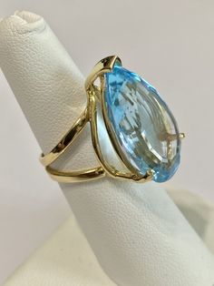 Stunning statement 14k yellow gold genuine blue topaz ring! This gorgeous ring contains a faceted pear cut genuine blue Topaz gemstone that weighs approximately 27.32 carats! The pear shaped gem is secured by 3 thick prongs. Incredible piece of fine jewelry featuring December birthstone! ERA - Modern, Estate METAL / MATERIAL - 14k yellow gold, 1 genuine Blue Topaz (approx. 27.32 cts) MARKINGS / HISTORY - Inside of ring is marked 14k CONDITION - Great vintage condition. SIZE / MEASUREMENTS - Size Fine Jewelry Yellow Gold Topaz Ring With Teardrop, Fine Jewelry Yellow Gold Topaz Teardrop Ring, Fine Blue Topaz Ring Pear-shaped, Formal Yellow Gold Topaz Teardrop Ring, Formal Blue Pear-shaped Topaz Ring, Formal Teardrop Blue Topaz Ring, Blue Topaz Teardrop Ring Fine Jewelry, Blue Topaz Teardrop Ring, Modern Estate