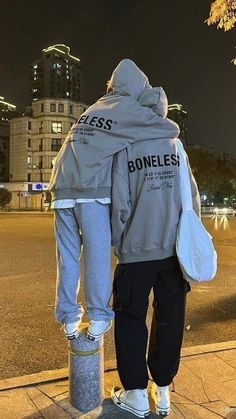 a man standing on the side walk with his back turned to the camera, wearing a jacket that says homeless