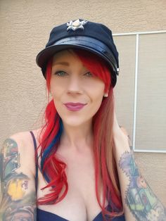 a woman with red hair wearing a hat and tattoos on her arm is posing for the camera