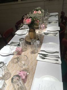 the table is set with silverware and pink flowers in vases on top of it