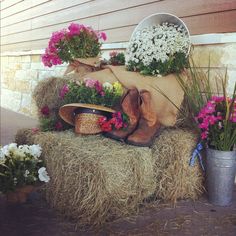 a hay bale with flowers and boots on it sitting in front of a house