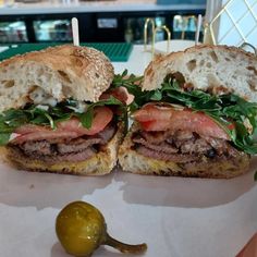 two sandwiches with meat, lettuce and tomato on them sitting on a table