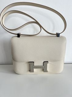 a white handbag sitting on top of a table next to a wall with the letter h