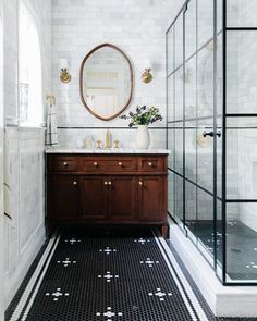 a bathroom with black and white tile flooring and a round mirror above the sink