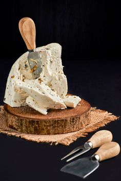 a piece of cheese on top of a wooden cutting board next to utensils