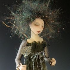 the doll is wearing a green dress with silver beads on it's head and her hair blowing in the wind