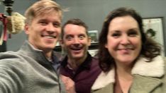 two men and a woman taking a selfie in front of a mirror with christmas decorations on the wall behind them