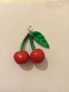 two cherries with green leaves hang from a metal hook on a white sheet paper