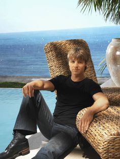 a man sitting in a wicker chair next to a swimming pool with the ocean in the background