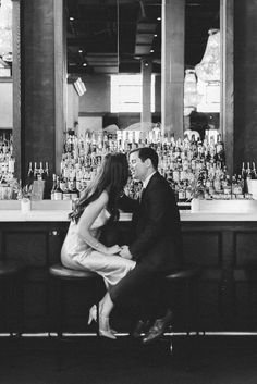 a man and woman sitting at a bar in front of liquor bottles on the counter