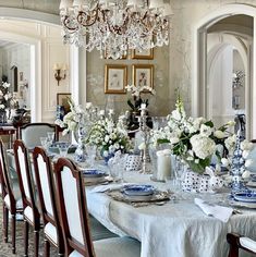 the dining room table is set with blue and white plates, silverware, and floral centerpieces