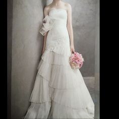 a woman in a white wedding dress holding a pink bouquet and posing for the camera