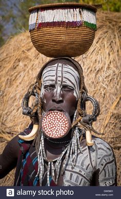 an african woman with painted face and headdress, carrying a basket on her head - stock image