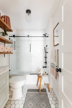 a white bathroom with black and white tiles on the floor, shower stall, toilet and shelving