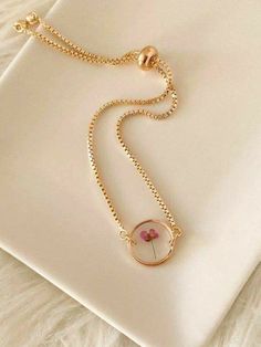 a necklace with a flower on it sitting on top of a white surface next to a gold chain