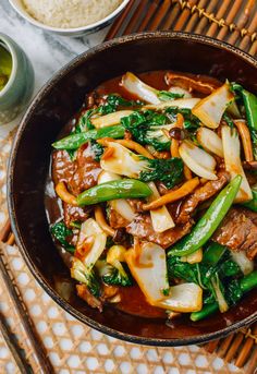 beef and vegetable stir fry in a brown bowl with chopsticks on the side