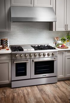 a stove top oven sitting inside of a kitchen next to white cabinets and wooden floors