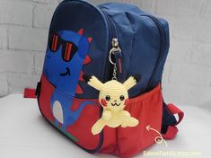 a backpack with a stuffed animal hanging from it's front pocket, on a table