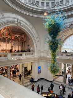 the interior of a building with people walking around and looking at art work hanging from the ceiling