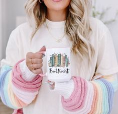 a woman is holding a coffee mug with books on it and she's wearing a colorful sweater