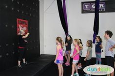 a group of young children standing on top of a black trampoline in a gym