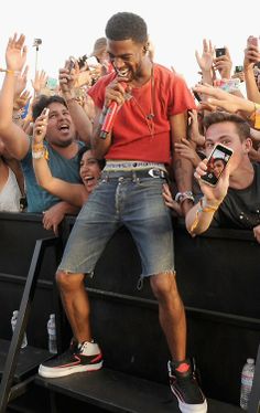 a man standing on the edge of a stage with his hands in the air while people take pictures