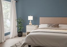 a bedroom with an orange accent wall and white curtains on the window sill, along with a bed