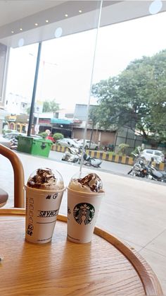 two cups of coffee sitting on top of a wooden table next to a glass window